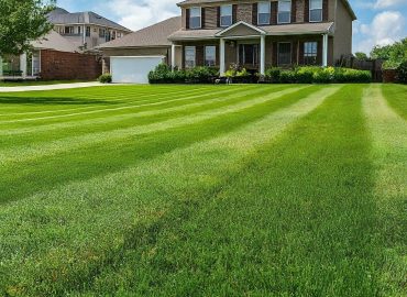Well-maintained two-story home with a covered front porch and a lush, striped green lawn in the foreground.