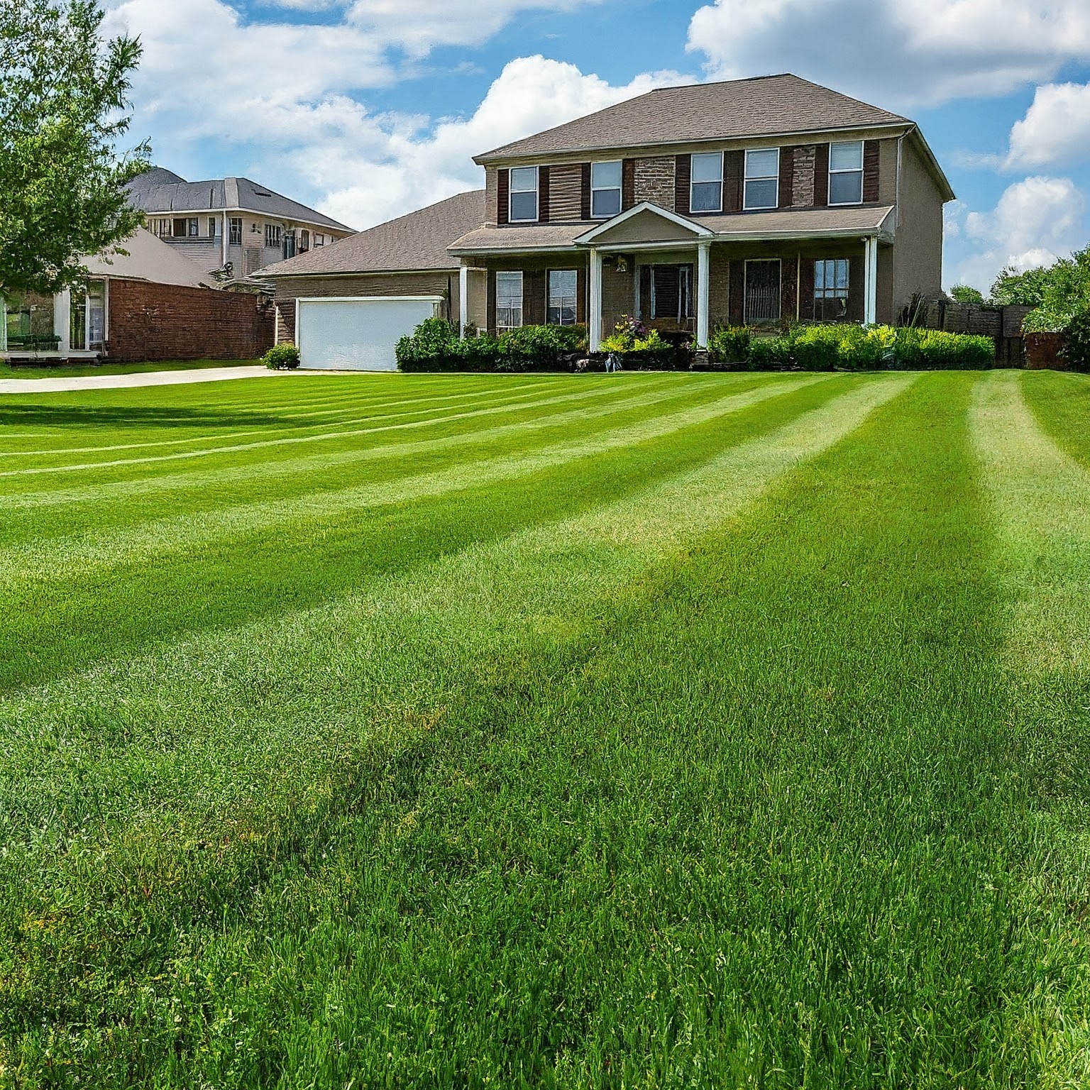Well-maintained two-story home with a covered front porch and a lush, striped green lawn in the foreground.